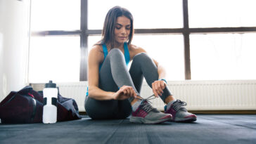 Uma mulher amarrando os sapatos na academia, demonstrando foco e preparação para o exercício. - Fitsse