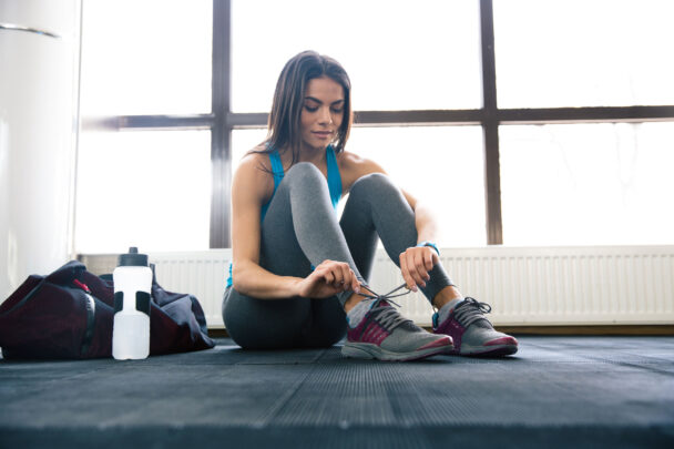 Uma mulher amarrando os sapatos na academia, demonstrando foco e preparação para o exercício. - Fitsse