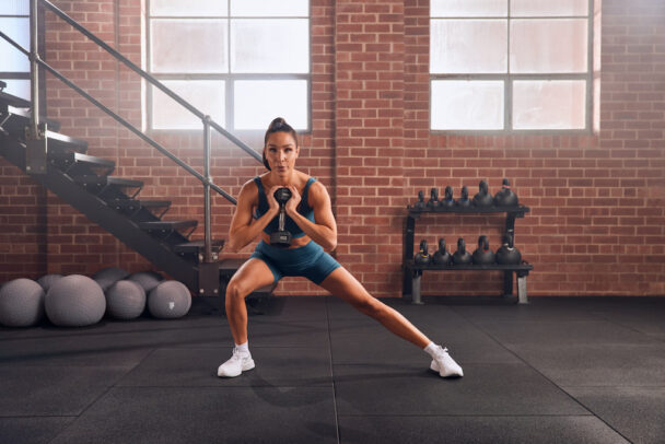 Mulher realizando agachamento em uma academia, focando na forma e na força muscular. - Fitsse