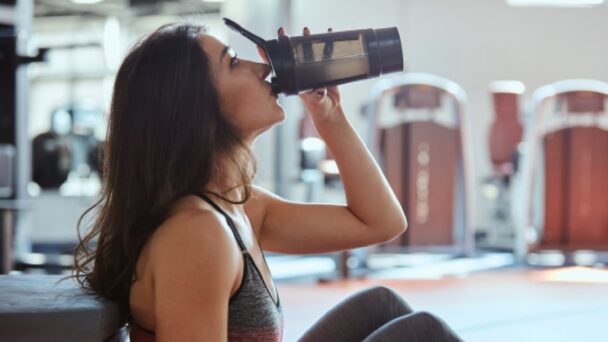 Mulher se hidratando com um shaker em uma academia, focada em seu treino e bem-estar. - Fitsse