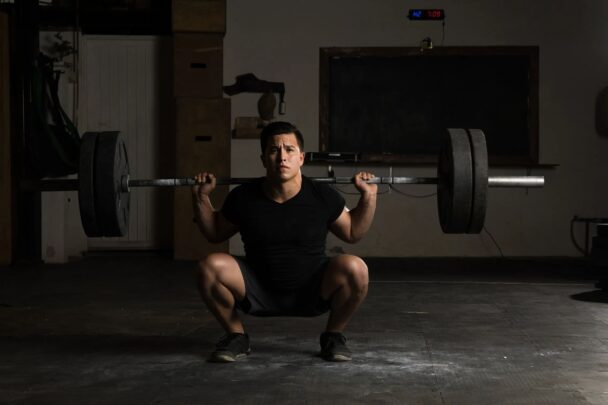 Homem realizando agachamento com barra em uma academia, focando na força e na técnica do exercício. - Fitsse