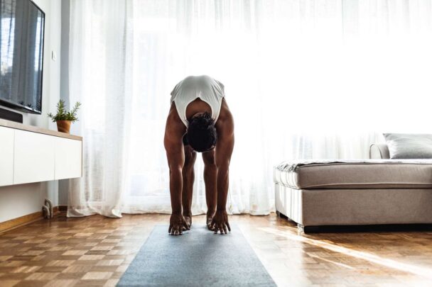 Pessoa praticando yoga em uma sala de estar, demonstrando equilíbrio e concentração em um ambiente acolhedor. - Fitsse